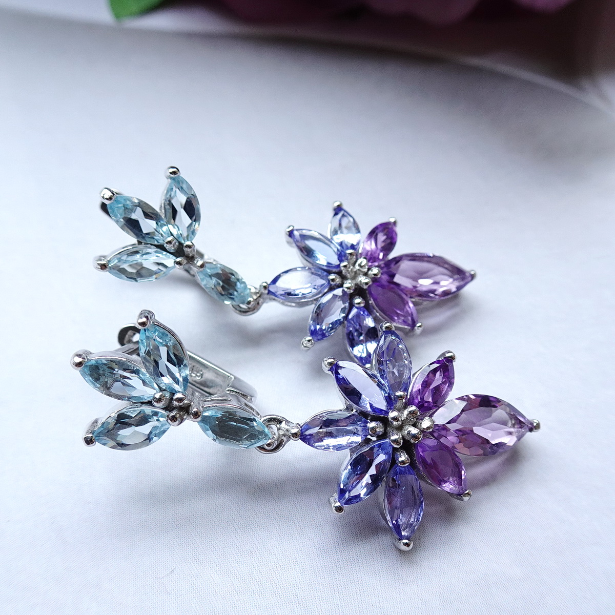 ต่างหูพลอยระย้าเฉดม่วงฟ้า เก๋ด้วยพลอยทรงมาคีทุกเม็ด ตัวเรือนฝังพลอยบลูโทพาสสีฟ้าใส ห้อยด้วยแทนซาไนท์สีม่วงอมฟ้าครามไล่เฉดไปม่วงอมชมพูอเมทิสท์ สวยหวานละมุน