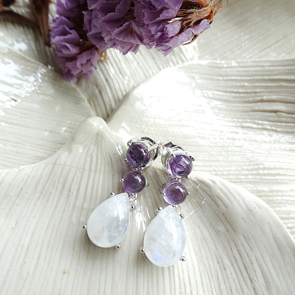 ต่างหูห้อยเรนโบว์มูนสโตน หรือมุกดาหารทรงลูกแพรหรือหยดน้ำ อัญมณีประจำราศีเมถุน ให้สีสะท้อนแสงเหลือบรุ้ง ด้านบนฝังอเมทิสท์สีม่วง ตัดกับสีขาวรุ้งของมูนสโตน สวยงามมากค่ะ