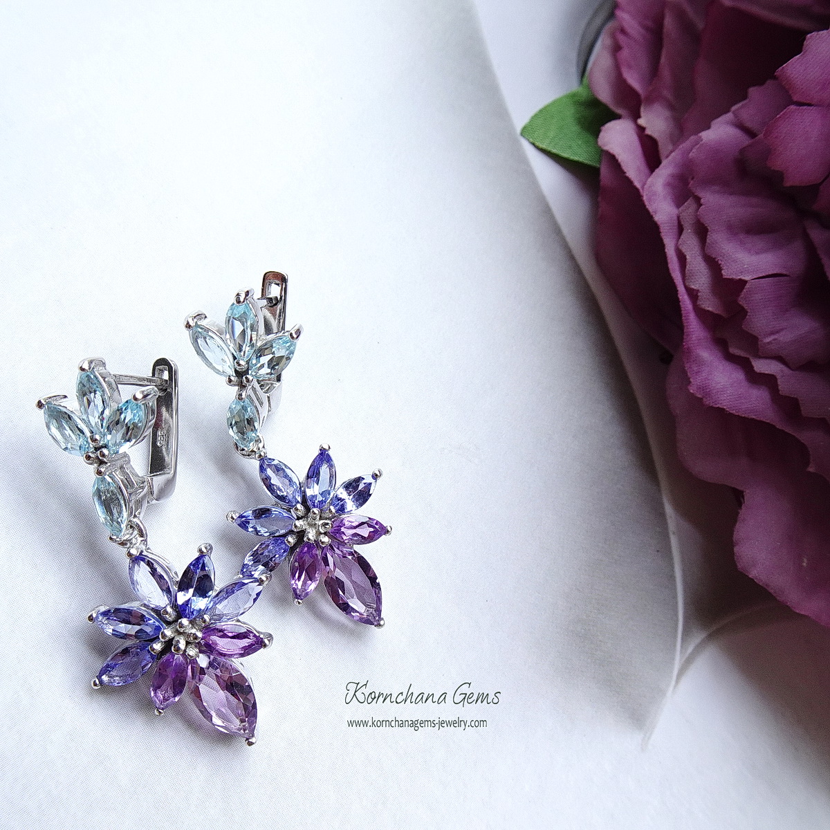 ต่างหูพลอยระย้าเฉดม่วงฟ้า เก๋ด้วยพลอยทรงมาคีทุกเม็ด ตัวเรือนฝังพลอยบลูโทพาสสีฟ้าใส ห้อยด้วยแทนซาไนท์สีม่วงอมฟ้าครามไล่เฉดไปม่วงอมชมพูอเมทิสท์ สวยหวานละมุน